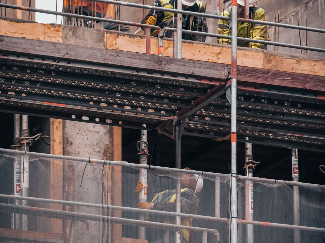Ouvriers casqués sur un échafaudage devant une structure en béton armé