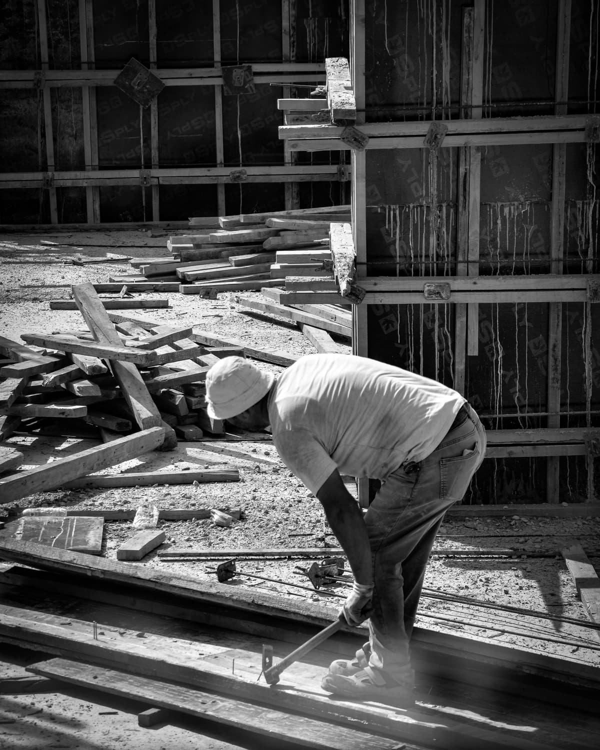 Charpentier assemblant un coffrage bois devant un mur banché, en noir et blanc