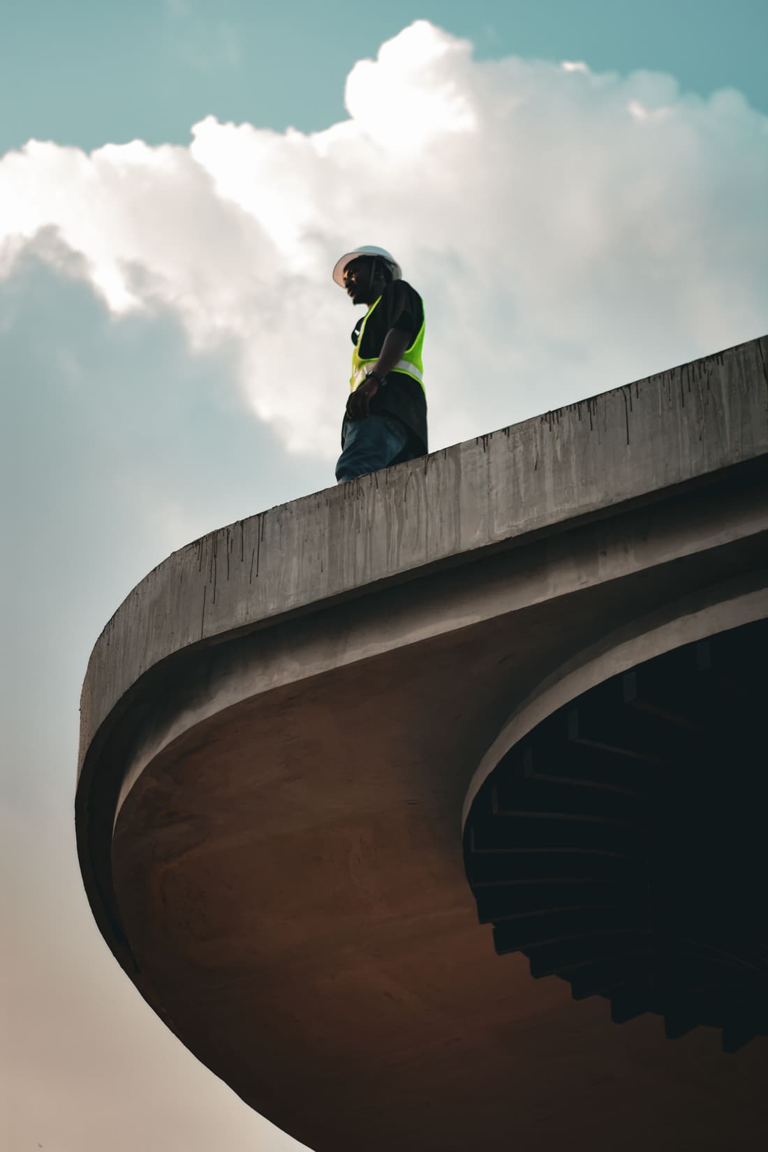 Ouvrier casqué en gilet de sécurité, debout au bord d’un ouvrage en béton courbe